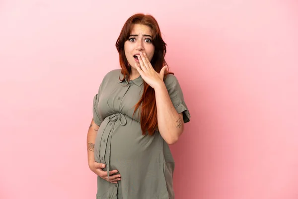 若いですRedhead Caucasian女性絶縁上のピンクの背景妊娠とやって驚きジェスチャー — ストック写真