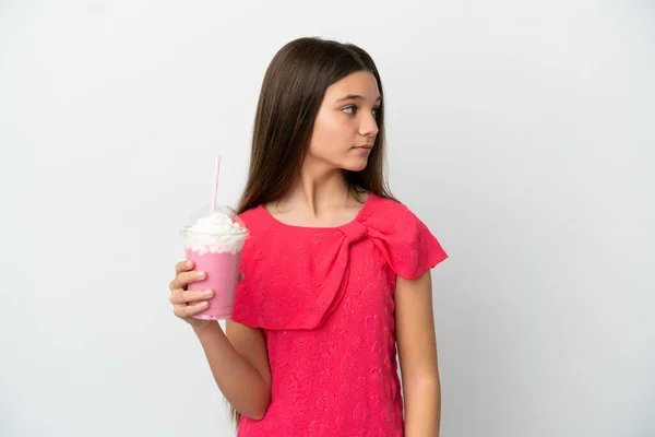 小さな女の子ともにイチゴミルクセーキ上の隔離された白い背景見ますザ側 — ストック写真