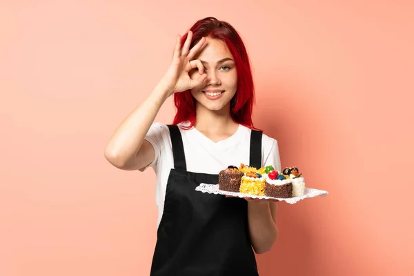 Pastelero Sosteniendo Muffins Aislado Sobre Fondo Rosa Mostrando Signo Con —  Fotos de Stock