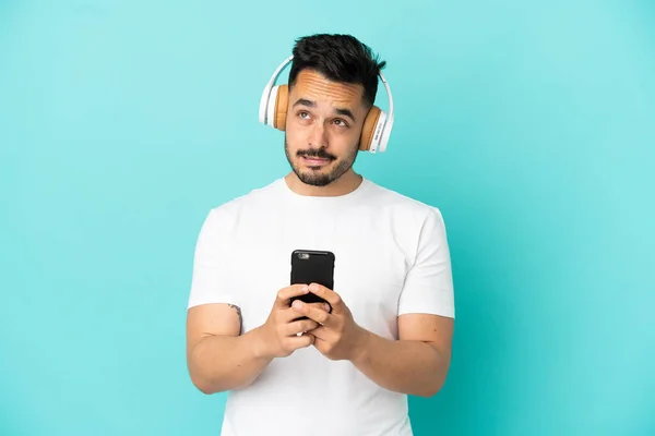 Νεαρός Καυκάσιος Άνδρας Απομονωμένος Μπλε Φόντο Ακούγοντας Μουσική Κινητό Και — Φωτογραφία Αρχείου