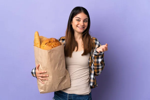 Молодая Женщина Держит Сумку Полную Хлеба Изолированы Фиолетовом Фоне Шокированным — стоковое фото