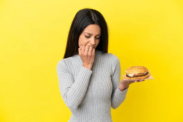 Young Caucasian Woman Holding Burger Isolated Yellow Background Having Doubts — Stock Photo, Image