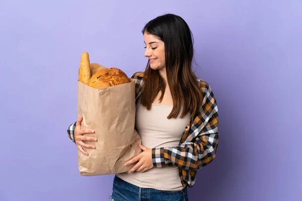 Jovem Segurando Saco Cheio Pães Isolados Fundo Roxo Com Expressão — Fotografia de Stock