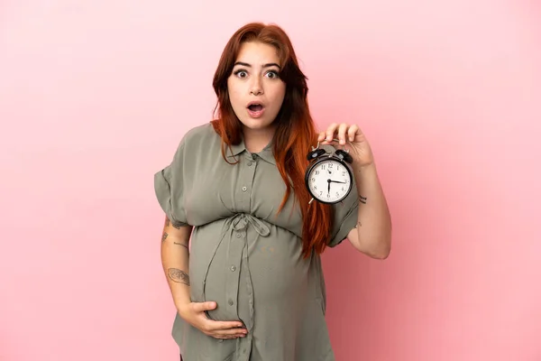 Młody Ruda Biały Kobieta Izolowane Różowy Tle Ciąży Trzymając Zegar — Zdjęcie stockowe