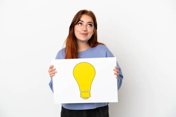 Young Redhead Woman Isolated White Background Holding Placard Bulb Icon — Stock Photo, Image