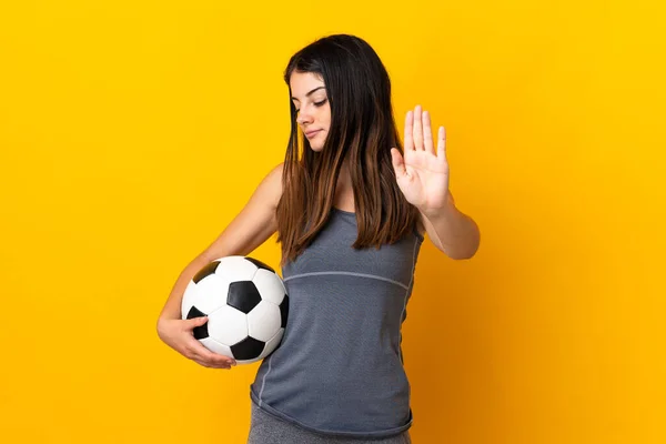 Young football player woman isolated on yellow background making stop gesture and disappointed