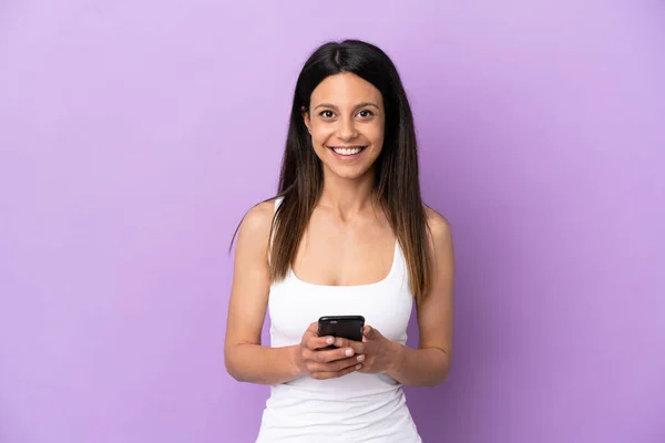 紫色の背景に孤立した若い白人女性が携帯電話でメッセージを送信 — ストック写真