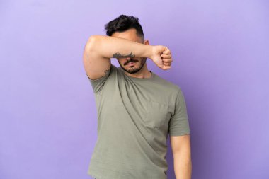Mor arka planda izole edilmiş genç beyaz adam gözleri elleriyle kapatıyor.