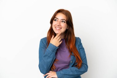 Genç kızıl saçlı kadın beyaz arka planda izole edilmiş gülümserken yukarı bakıyor.
