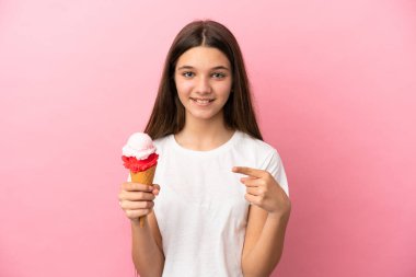 Kornet dondurması olan küçük bir kız pembe arka planda bir ürün sunmak için kenarı işaret ediyor.