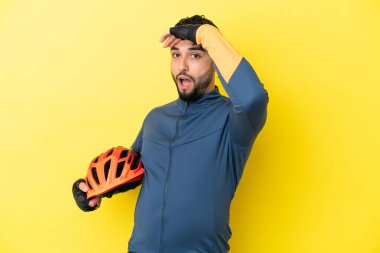 Genç bisikletçi Arap, sarı arka planda izole edilmiş. Yan tarafa bakarken sürpriz jest yapıyor.
