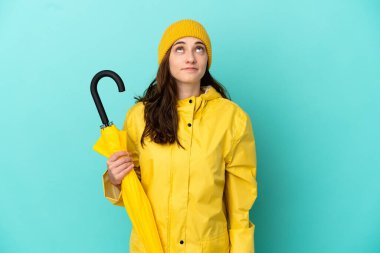 Mavi arka planda şemsiye tutan genç beyaz bir adam var.