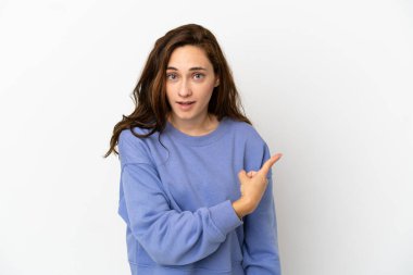 Beyaz arka planda izole edilmiş genç beyaz kadın şaşırmış ve işaret ediyor.