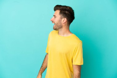 Beyaz tenli yakışıklı adam mavi arka planda izole edilmiş. Yan pozisyonda gülüyor.