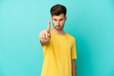Beyaz tenli yakışıklı adam mavi arka planda izole edilmiş ciddi bir ifadeye sahip birini sayıyor.