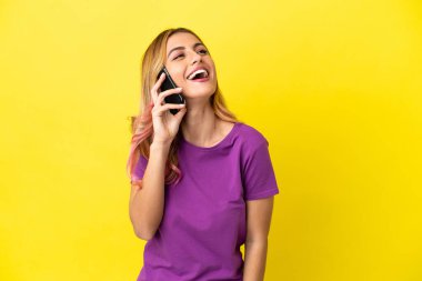 İzole edilmiş sarı arka planda cep telefonu kullanan genç kadın gülüyor.
