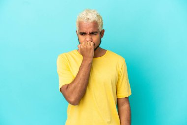 Genç Kolombiyalı yakışıklı adam mavi arka planda izole edilmiş. Şüpheleri var.