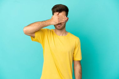 Beyaz tenli yakışıklı bir adam mavi arka planda tek başına, gözleri elleriyle kapatıyor. Bir şey görmek istemiyorum.