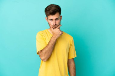 Kafkasyalı yakışıklı genç adam mavi arka planda izole edilmiş şüpheleri var.