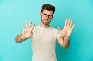 Beyaz tenli yakışıklı adam mavi arka planda izole edilmiş dokuz parmaklı sayıyor.