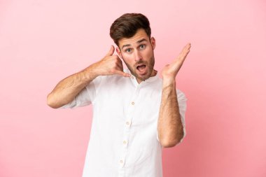 Beyaz tenli yakışıklı adam pembe arka planda izole edilmiş telefon jestleri yapıyor ve şüpheli.