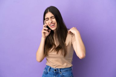 Mor arka planda cep telefonu kullanan, omuz ağrısı çeken genç beyaz bir kadın gayret gösterdiği için acı çekiyor.