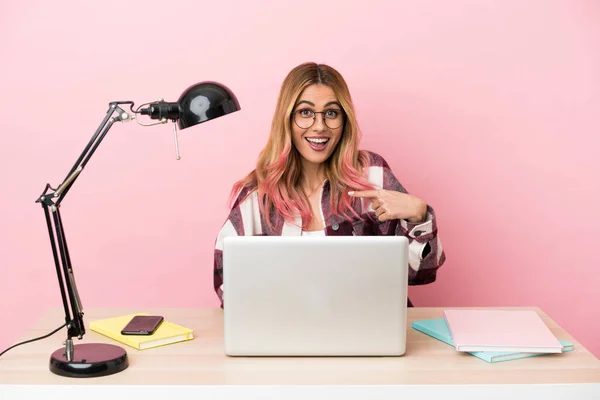 Young student woman in a workplace with a laptop over pink background with surprise facial expression
