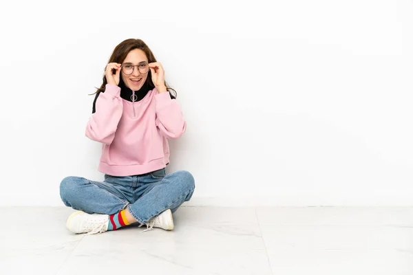 Mladá Běloška Žena Sedí Podlaze Izolované Bílém Pozadí Brýlemi Překvapen — Stock fotografie