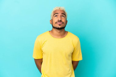 Genç Kolombiyalı yakışıklı adam mavi arka planda izole edilmiş ve yukarı bakıyor.