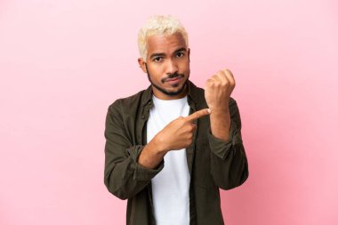 Pembe arka planda izole edilmiş genç Kolombiyalı yakışıklı adam geç kalma jesti yapıyor.