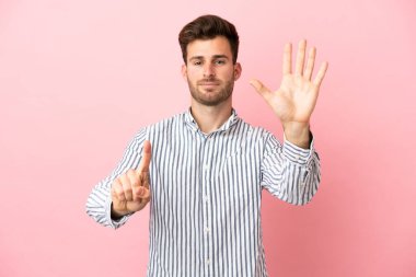 Pembe arka planda izole edilmiş beyaz, yakışıklı genç adam parmaklarıyla altısını sayıyor.