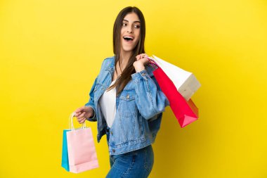 Mavi arka planda izole edilmiş genç beyaz bir kadın alışveriş torbaları tutuyor ve gülümsüyor.