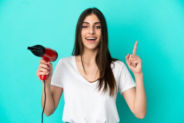 Mavi arka planda saç kurutma makinesi tutan beyaz bir kadın harika bir fikre işaret ediyor.
