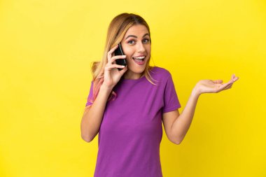 İzole edilmiş sarı arka planda cep telefonu kullanan genç bir kadın.