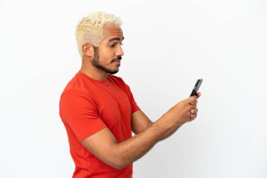 Beyaz arka planda izole edilmiş genç Kolombiyalı yakışıklı cep telefonuyla mesaj ya da e-posta yolluyor.