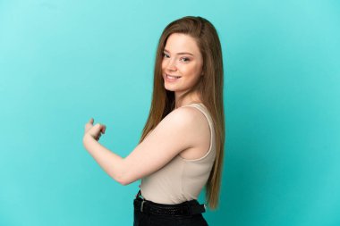 İzole edilmiş mavi arka planı olan genç kız geriye doğru işaret ediyor.