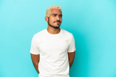 Genç Kolombiyalı yakışıklı adam mavi arka planda izole edilmiş.