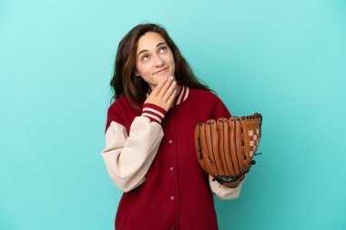 Beyzbol oynayan beyaz bir kadın mavi arka planda izole edilmiş gülümserken yukarı bakıyor.