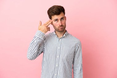 Genç, beyaz, yakışıklı bir adam pembe arka planda izole edilmiş ve intihar jesti yapmada sorun yaşıyor.