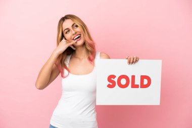 Soyutlanmış pembe arka planı olan genç bir kadın. Elinde yazılı bir pankart tutuyor ve gelecek vaadeden bir jest yapıyor.