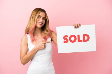 Soyutlanmış pembe arka planı olan genç bir kadın elinde bir pankart tutuyor ve onu işaret ediyor.