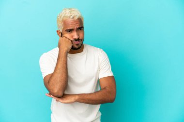 Genç Kolombiyalı yakışıklı adam mavi arka planda izole edilmiş, yorgun ve sıkılmış bir ifadeyle.