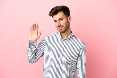 Beyaz tenli yakışıklı adam pembe arka planda izole edilmiş, mutlu bir ifadeyle selamlanıyor.