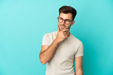 Beyaz tenli yakışıklı adam mavi arka planda izole edilmiş, yana bakıyor ve gülümsüyor.