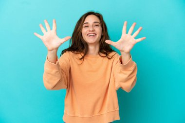 Mavi arka planda izole edilmiş genç beyaz kadın parmaklarıyla ona kadar sayıyor.