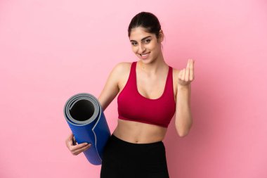 Genç beyaz kadın, elinde hasırla yoga derslerine gidiyor. Para hareketi yapıyor.