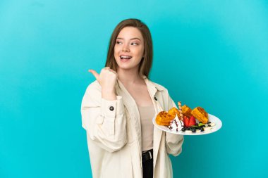 İzole edilmiş mavi arka plan üzerinde waffle tutan genç kız çözümü bulmak için bir parmağını kaldırarak