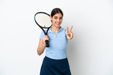 Yakışıklı genç tenisçi beyaz arka planda izole edilmiş beyaz kadın gülümsüyor ve zafer işareti gösteriyor.