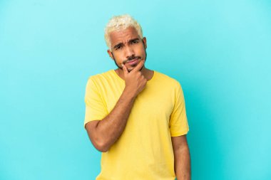 Genç Kolombiyalı yakışıklı adam mavi arka planda izole edilmiş. Şüpheleri var.
