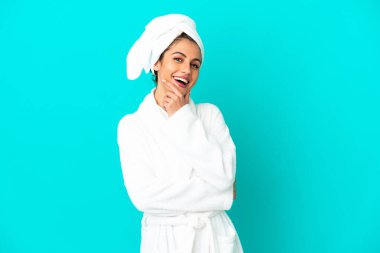 Bornozlu genç bir kadın mavi arka planda mutlu ve gülümsüyor.